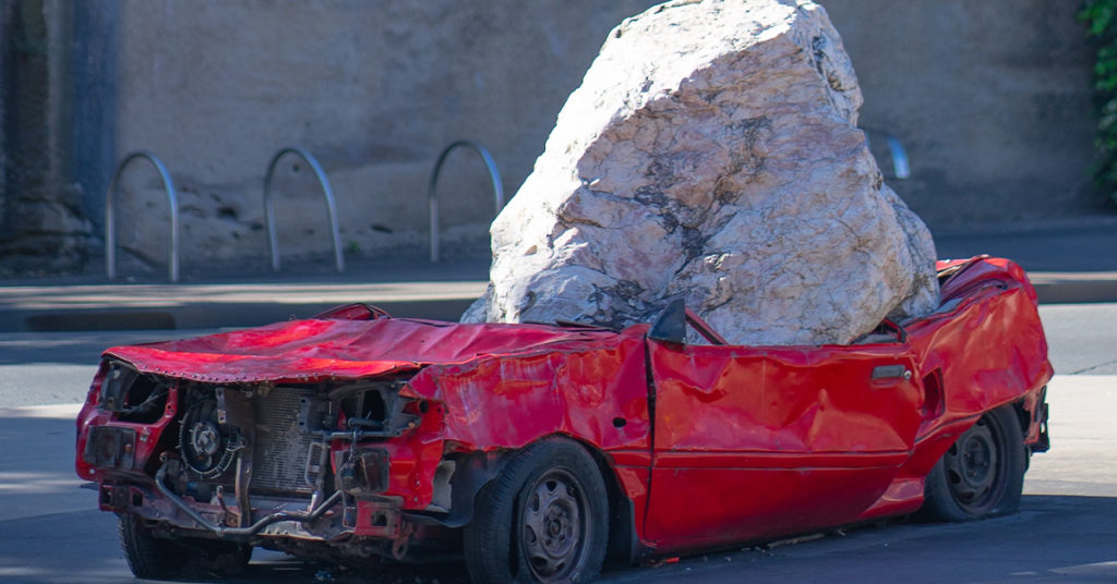 large rock crushed red car
